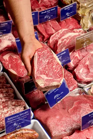 Hand holding a dry-aged beef steak at a butcher counter.