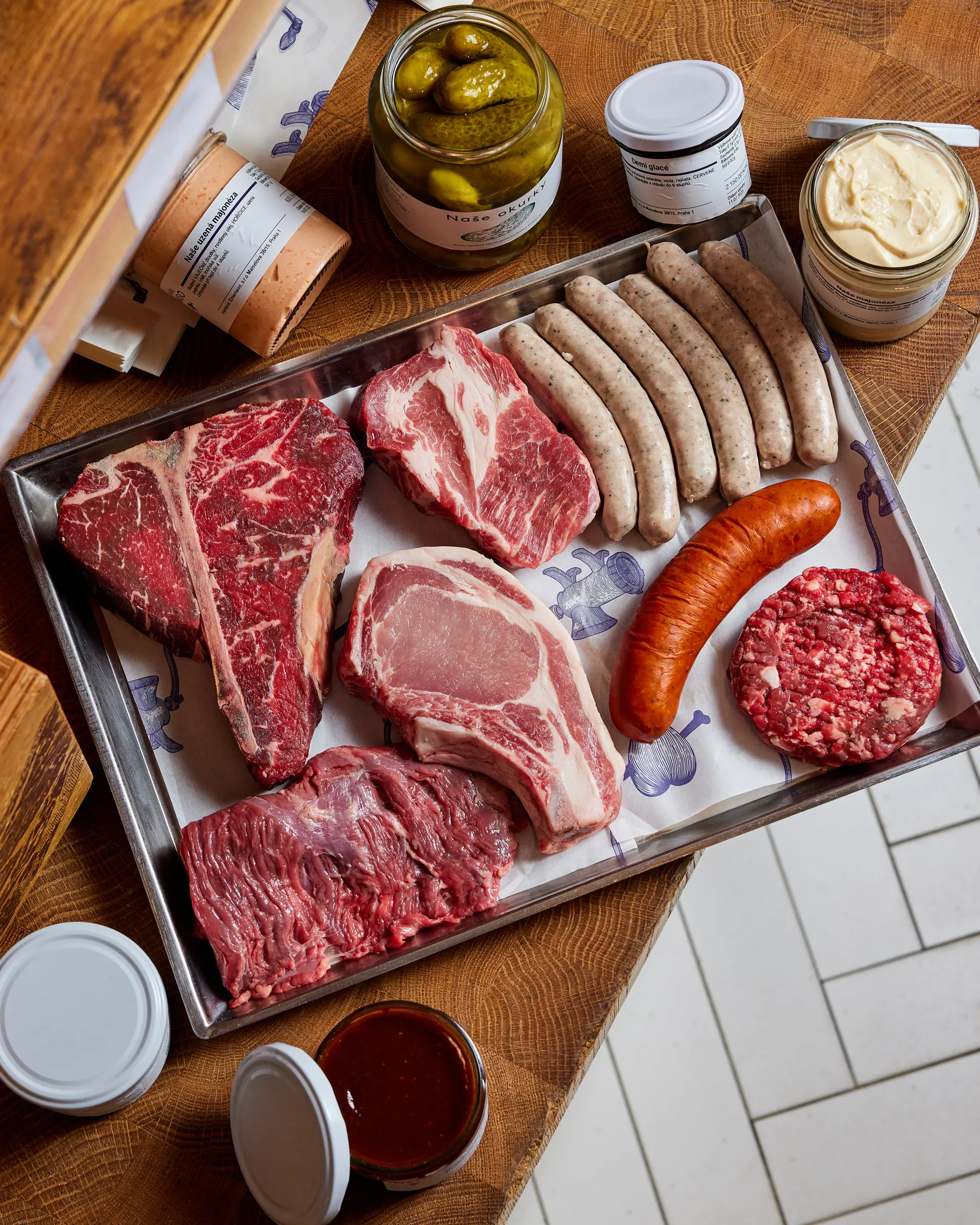 Selection of meat cuts, sausages, and deli items on a tray.