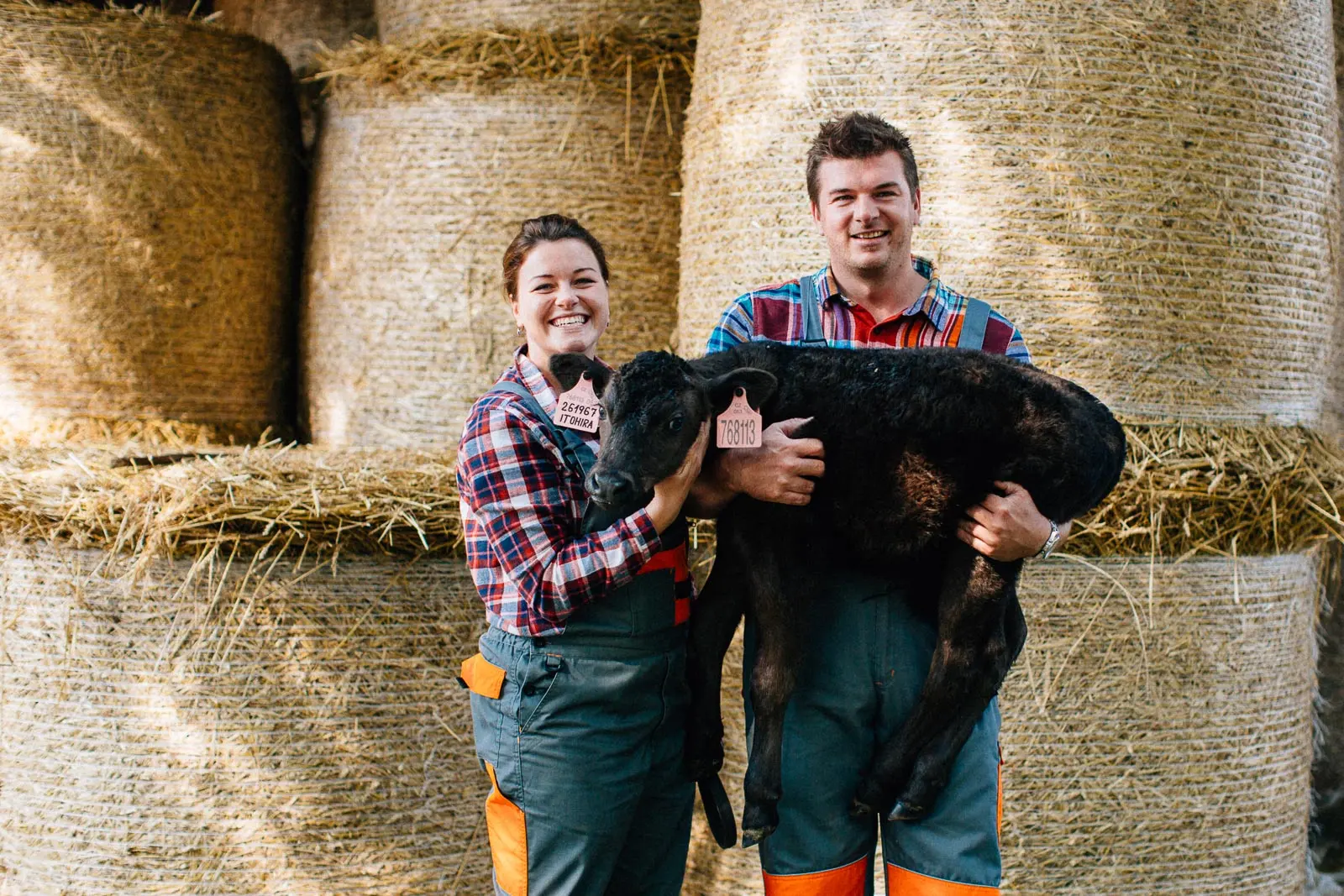 Young farming couple holding a calf in front of hay bales.