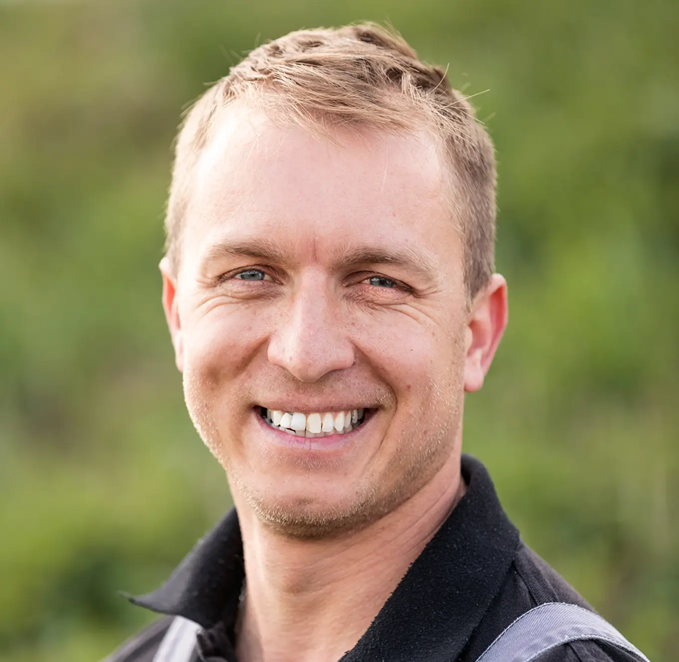 Smiling man in workwear with a green background.